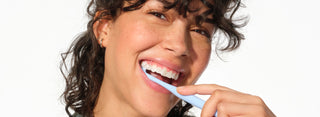 Woman brushing her teeth with a blue toothbrush on a white background