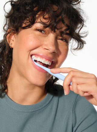 Woman brushing her teeth with a blue toothbrush on a white background